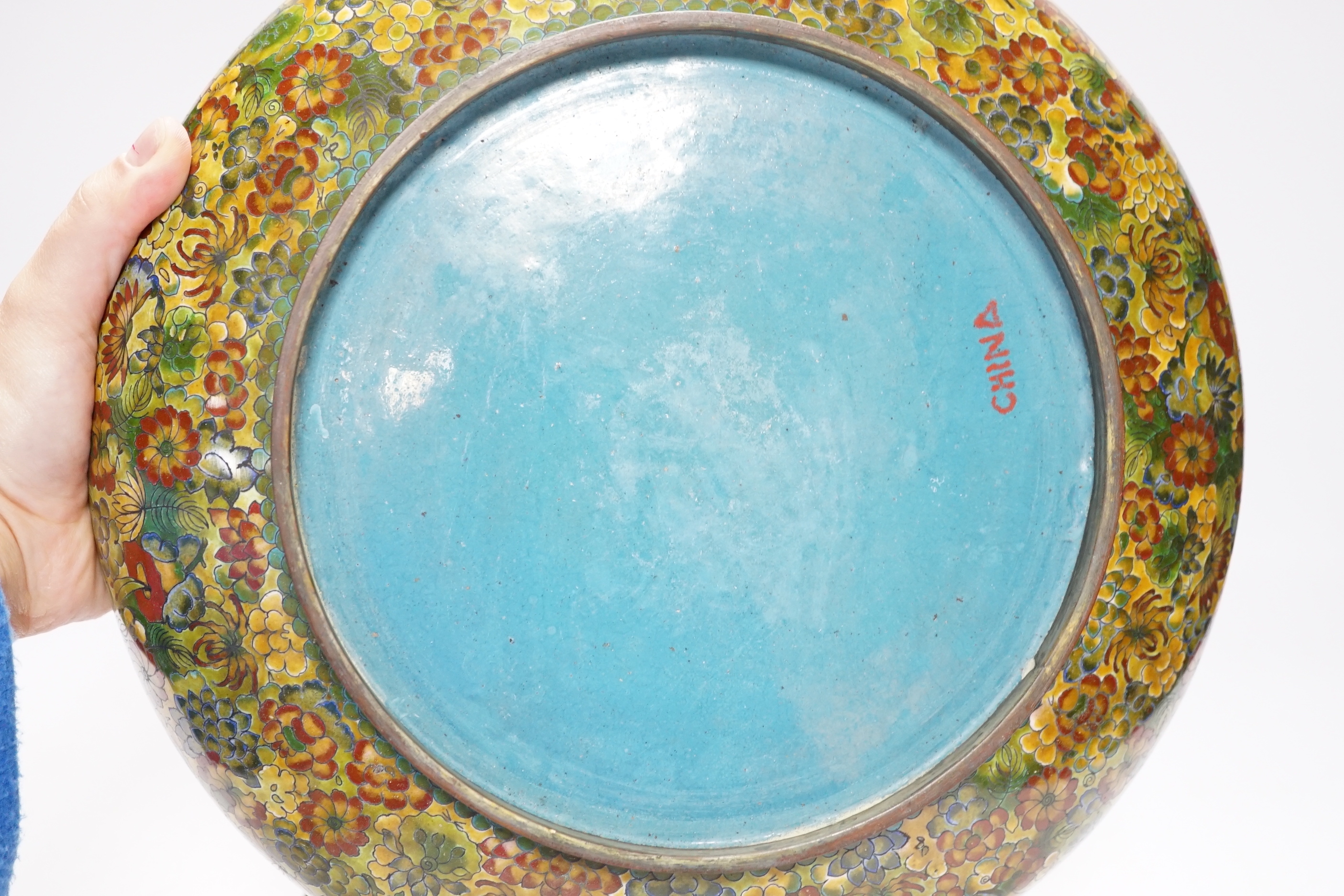 A Chinese circular cloisonné enamel bowl decorated with multi-coloured flowerheads on wooden stand, 30cm diameter